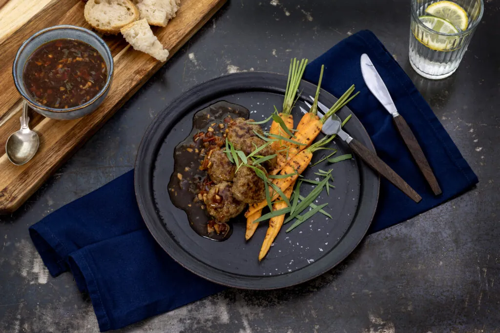 en mattsvart tallrik med köttbullar och orangea morötter fint upplagt
