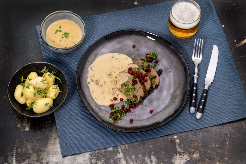 En tallrik med köttfärslimpa, röda lingon och ljus sås