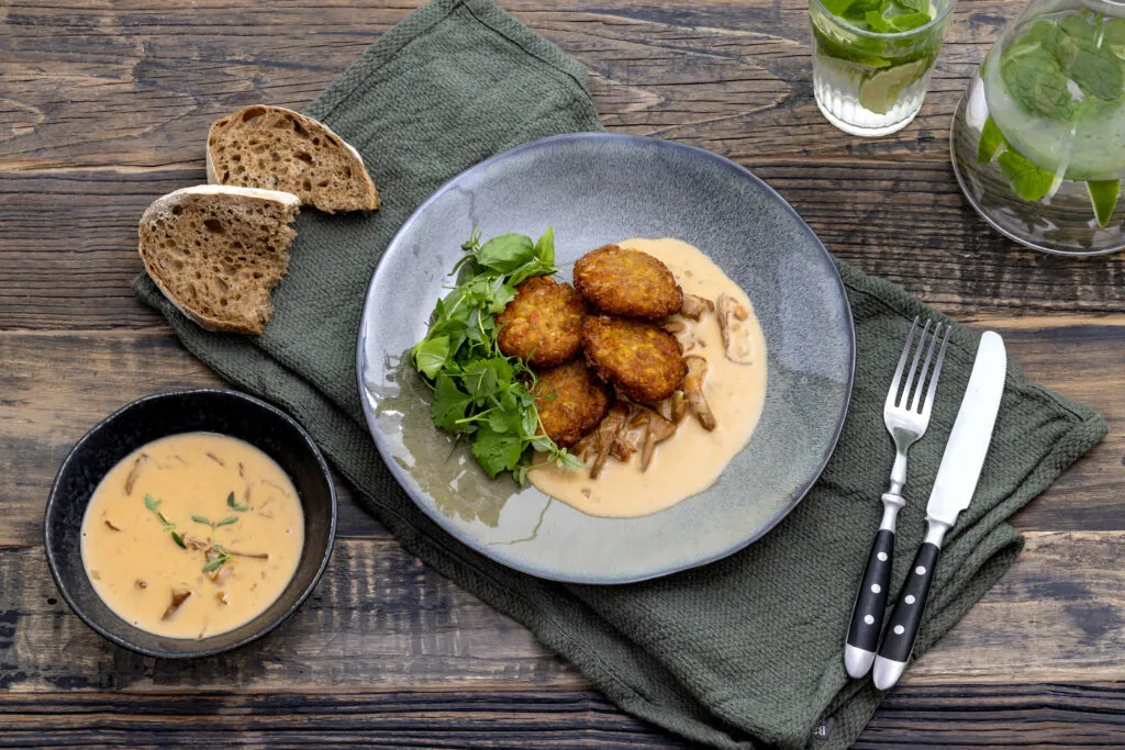 En grå porslinstallrik med majsbiffar och kantarellsås.