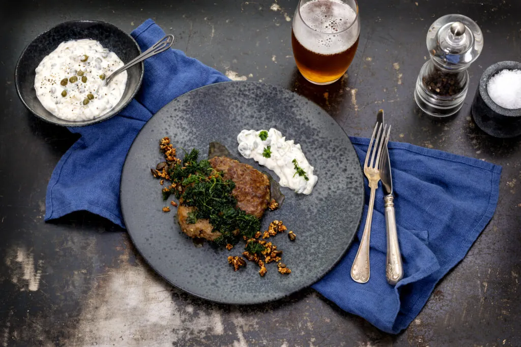 en tallrik med en pannbiff dekorerad med gröna örter och en vit sås