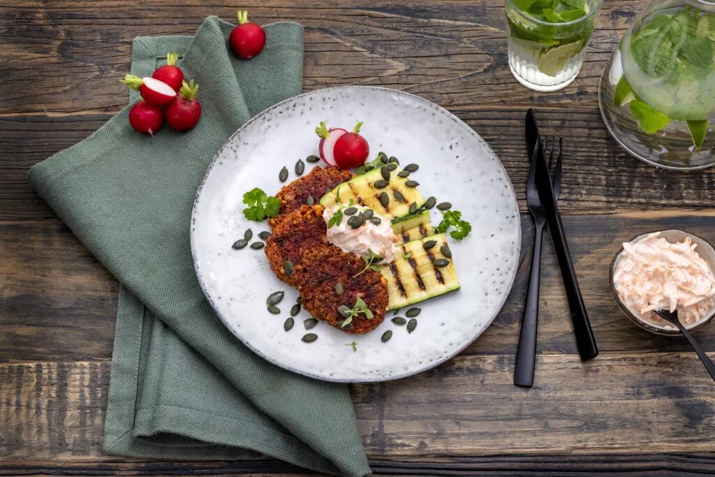 En bordsdukning med en tallrik med mat på som innehåller Halloumi och rödbetsbiffar och grillad Zucchini